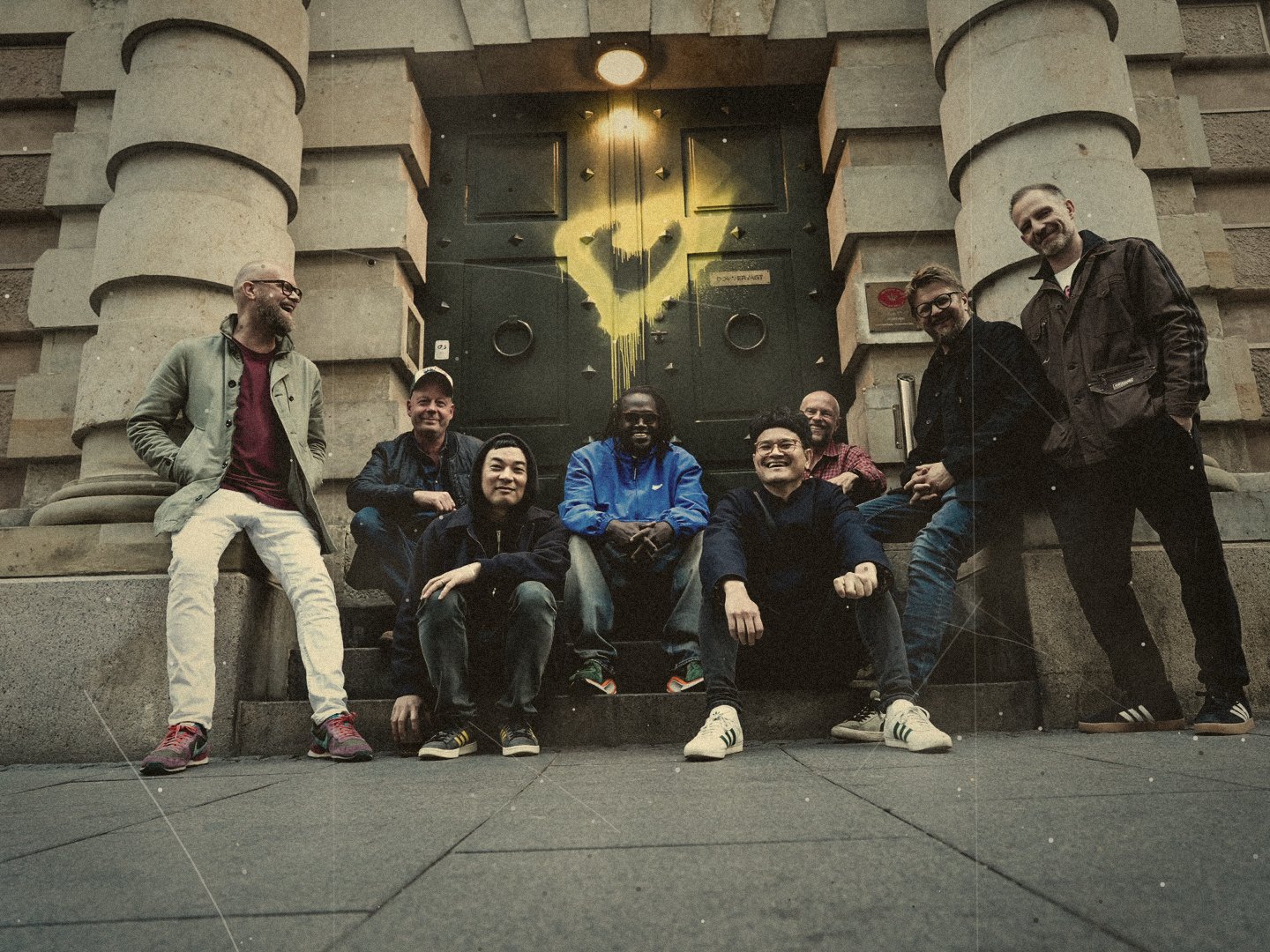 The 5to8s band members smiling on stone steps in front of a green door
